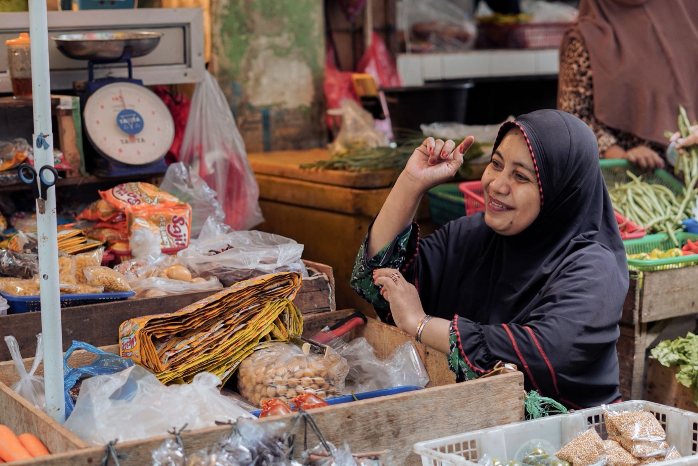 A smiling market vendor in a hijab at her stall